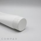 A close-up of a white, cylindrical squeeze tube with a matching white cap lying on its side. The background is plain light grey. The product name "60mm Flip Top" and the brand name "COMPAX" are visible in the bottom left corner of the image.