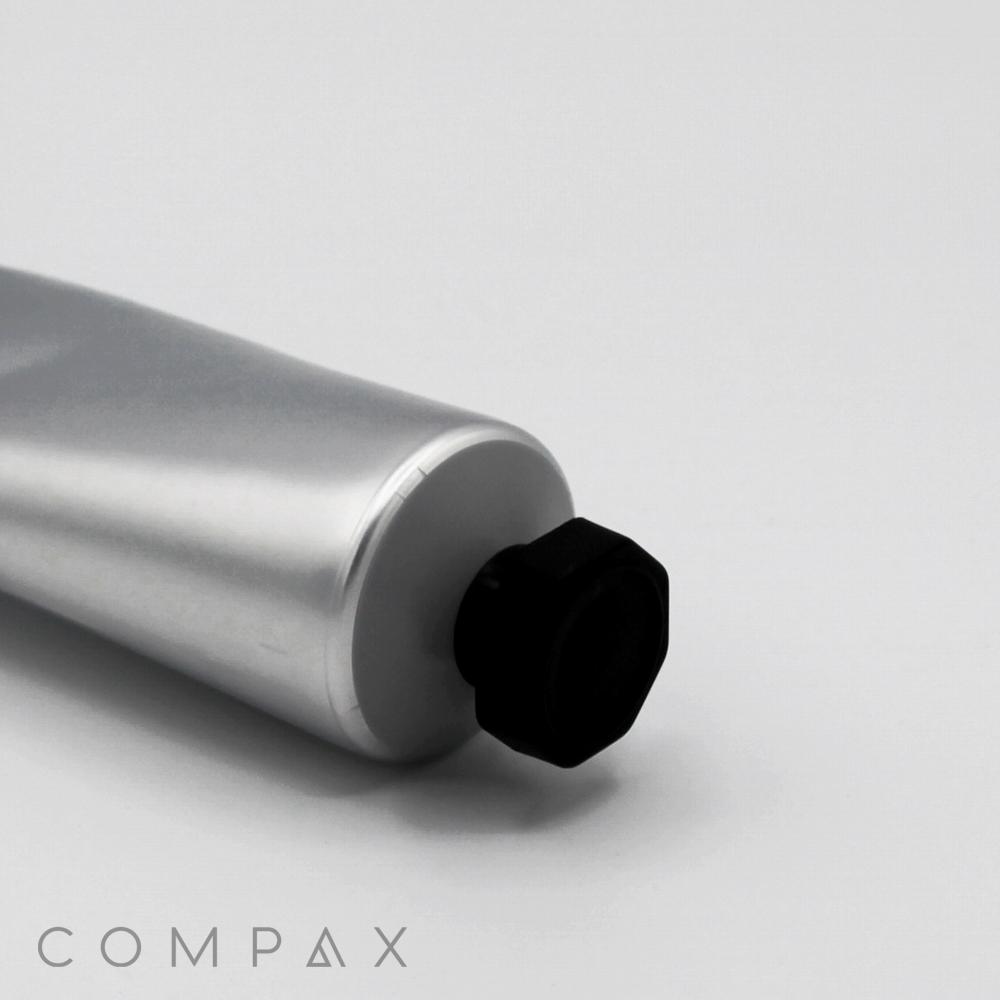 A close-up of a silver tube labeled "40mm Screw Top" with a black cap on a plain white background. The tube is angled diagonally with the cap visible in the lower right corner. The word "COMPAX" is faintly visible in the bottom left corner.