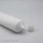 A white 40mm Needle Nose cylindrical tube with its cap removed, laying horizontally on a light grey surface. The tube's dispensing nozzle is visible, and the cap is placed beside it. The word "COMPAX" is subtly printed in the bottom left corner.