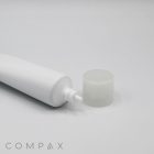 A close-up image of a white squeeze tube labeled "30mm Needle Nose" with a clear, round cap placed beside it on a white surface. The tube appears to be made of plastic and is empty. The word "COMPAX" is visible in small text at the bottom left corner.