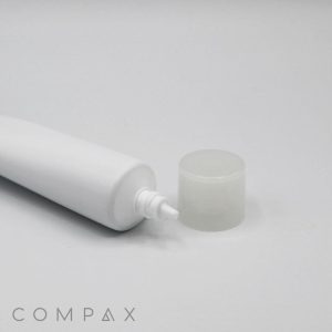 A close-up image of a white squeeze tube labeled "30mm Needle Nose" with a clear, round cap placed beside it on a white surface. The tube appears to be made of plastic and is empty. The word "COMPAX" is visible in small text at the bottom left corner.