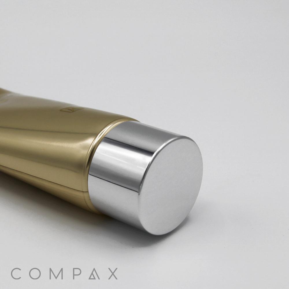 A close-up image of a golden 40mm Screw Top with a silver cap, lying horizontally on a gray surface. The brand name "COMPAX" is visible in gray text at the bottom left corner of the image.