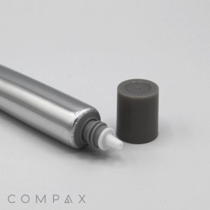 A 19mm Needle Nose, a silver cylindrical object with a white nozzle at one end and a dark grey cap removed and placed to the side, all set against a white background. The word "COMPAX" is visible in light grey text at the bottom left corner of the image.