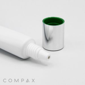 A white plastic tube with its nozzle exposed and a silver cap placed next to it, revealing a green interior. The word "COMPAX" is visible in the bottom left corner of the image, which features the 19mm Needle Nose against a plain white background.