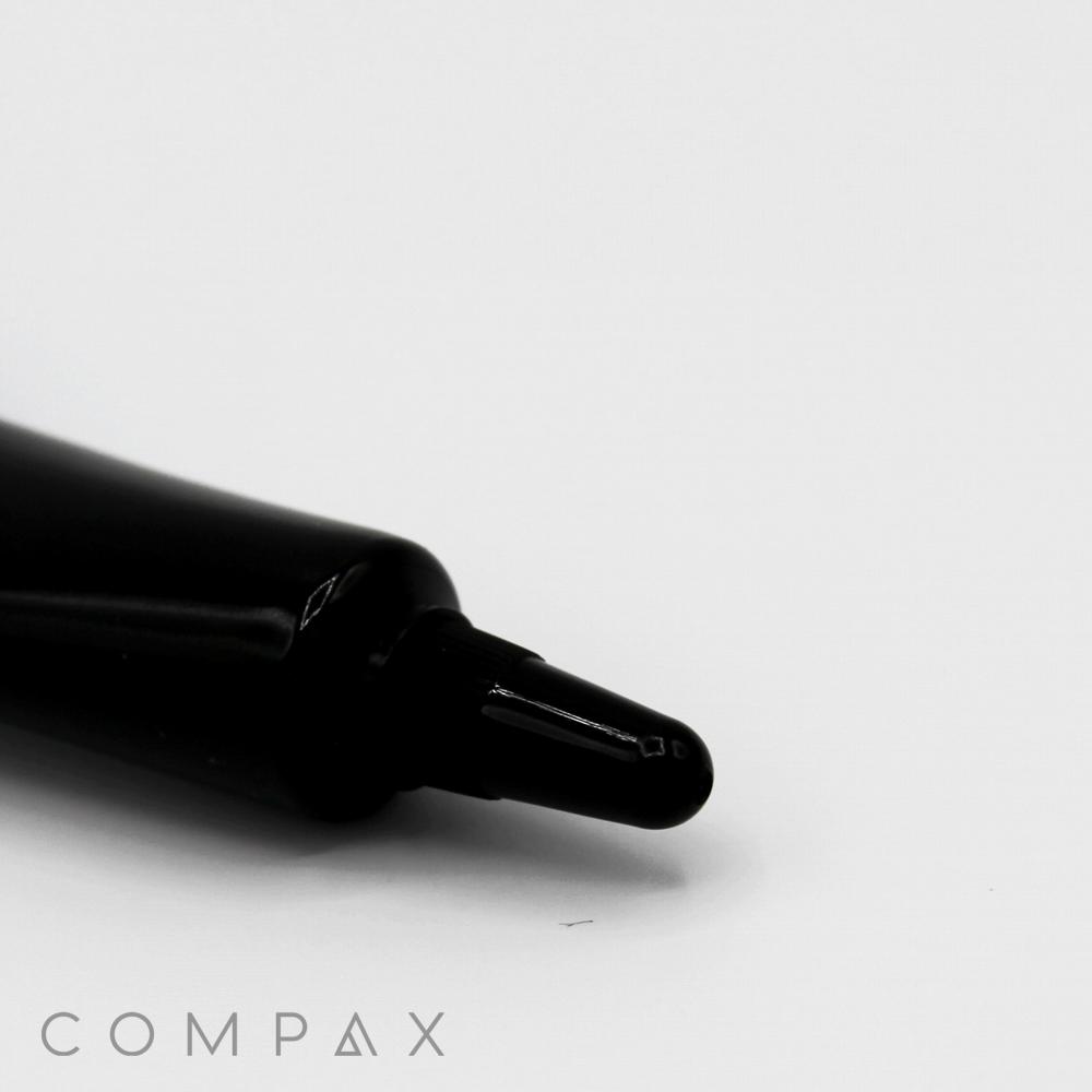 A black 16mm Needle Nose lies horizontally on a white surface, with the marker tip prominently in focus. The word "COMPAX" is written in lowercase letters in the bottom left corner of the image.