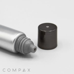 A close-up image of a gray and silver metallic 16mm Screw Top with a rounded dispensing tip and a small black cap placed beside it on a flat surface. The word "COMPAX" is printed at the bottom of the image.