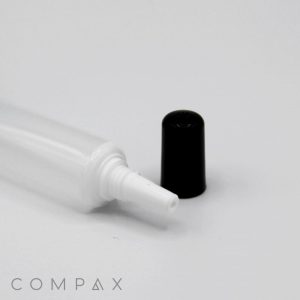 A close-up image of a white plastic tube labeled "16mm Needle Nose" with an open nozzle, laying horizontally on a white surface. The tube's black cap is placed beside it. The word "COMPAX" is lightly visible in the bottom left corner.