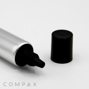 A silver tube, labeled "22mm Needle Nose," lies horizontally with its black cap removed and placed beside it. The tube's nozzle is visible, and the name "COMPAX" is displayed in the bottom-left corner. The background is plain white.