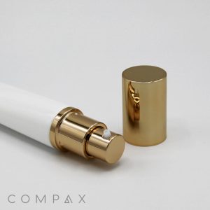 A 25mm Airless white and gold cylindrical spray bottle is displayed with its gold cap removed and placed next to it on a white surface. The brand name "COMPAX" is visible in the bottom left corner of the image.