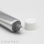 A silver tube marked "25mm Screw Top" with a white cap beside it sits on a white background. The sealed appearance of the tube indicates it is unused. The name "COMPAX" is printed in grey at the bottom left corner of the image.