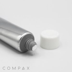 A silver tube marked "25mm Screw Top" with a white cap beside it sits on a white background. The sealed appearance of the tube indicates it is unused. The name "COMPAX" is printed in grey at the bottom left corner of the image.