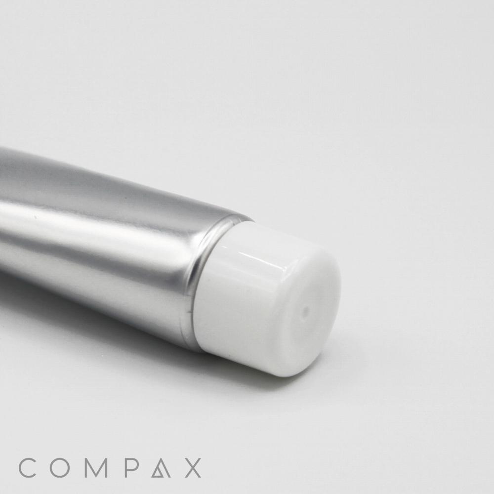 A close-up view of a silver aluminum tube labeled "25mm Screw Top" with a white cap on a plain white background. The bottom right corner of the image features the word "COMPAX" in gray, stylized text.