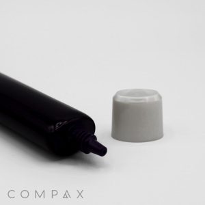 A black 25mm Oval Needle Nose with a small nozzle is lying horizontally on a white surface. The gray-colored cap, which was previously on the nozzle, is also on the surface to the right of it. The word "COMPAX" is written in light gray at the bottom left corner.
