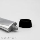 A silver tube labeled "35mm Oval Screw Top" with a screw-on black cap, slightly open at the nozzle, is positioned against a plain white background. The brand name "COMPAX" is visible in gray letters at the bottom left corner.