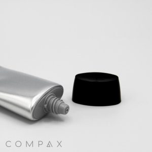 A silver tube labeled "35mm Oval Screw Top" with a screw-on black cap, slightly open at the nozzle, is positioned against a plain white background. The brand name "COMPAX" is visible in gray letters at the bottom left corner.