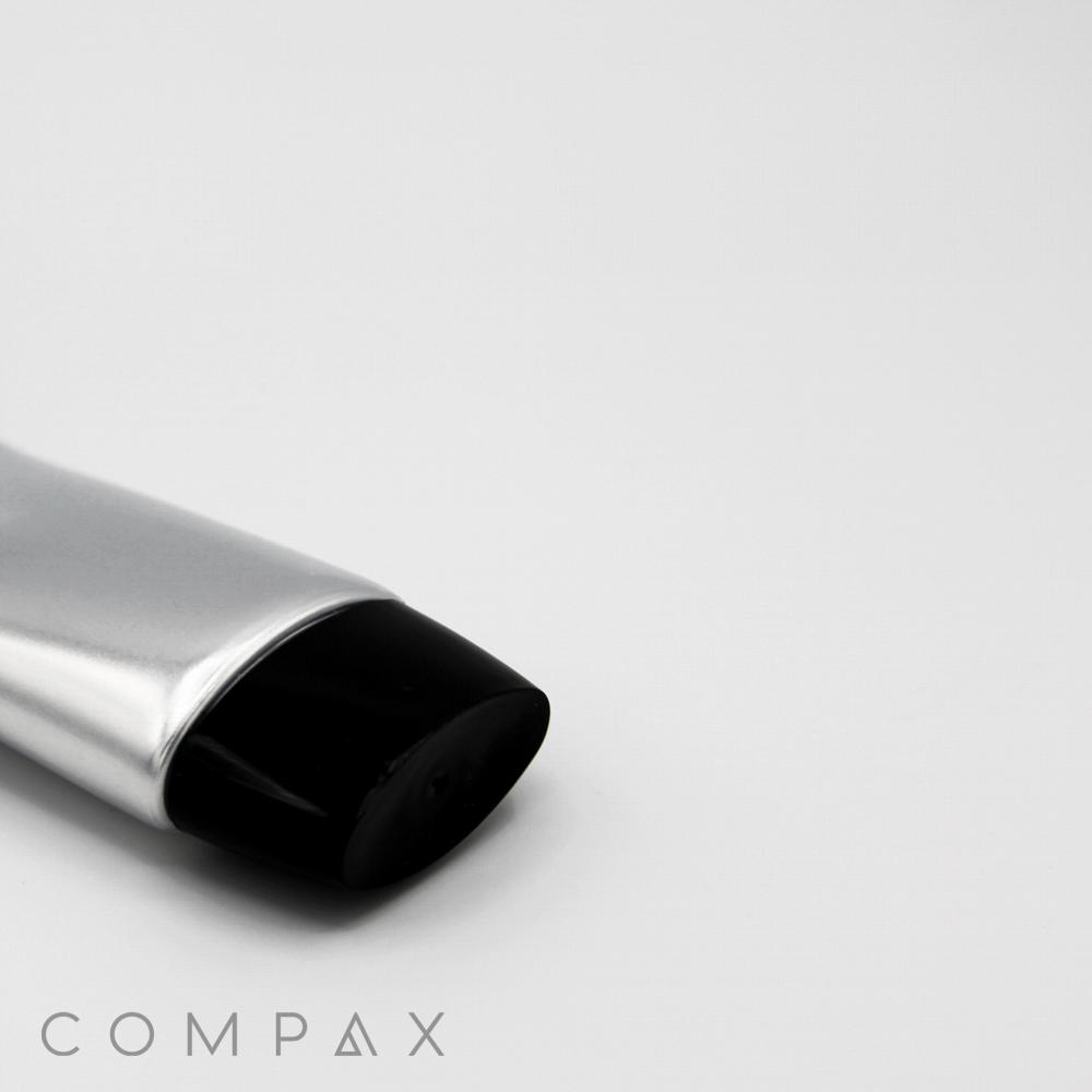 A close-up photo of a 35mm Oval Screw Top, featuring a silver tube with a black cap, positioned at an angle against a plain white background. The word "COMPAX" is visible in gray text at the bottom-left corner.