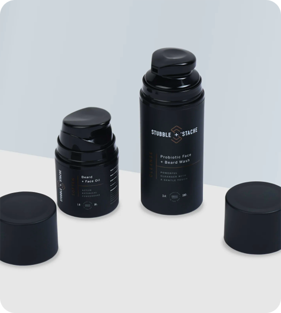 Two black airless pump bottles with their caps removed and placed beside them. The right bottle is taller than the left.