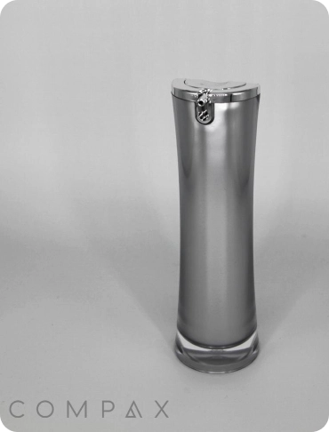 A sleek, cylindrical airless pump bottle with a metallic silver finish stands upright against a simple, light-gray background. The text "COMPAX" appears at the bottom of the image. The bottle features a locking mechanism at the top.