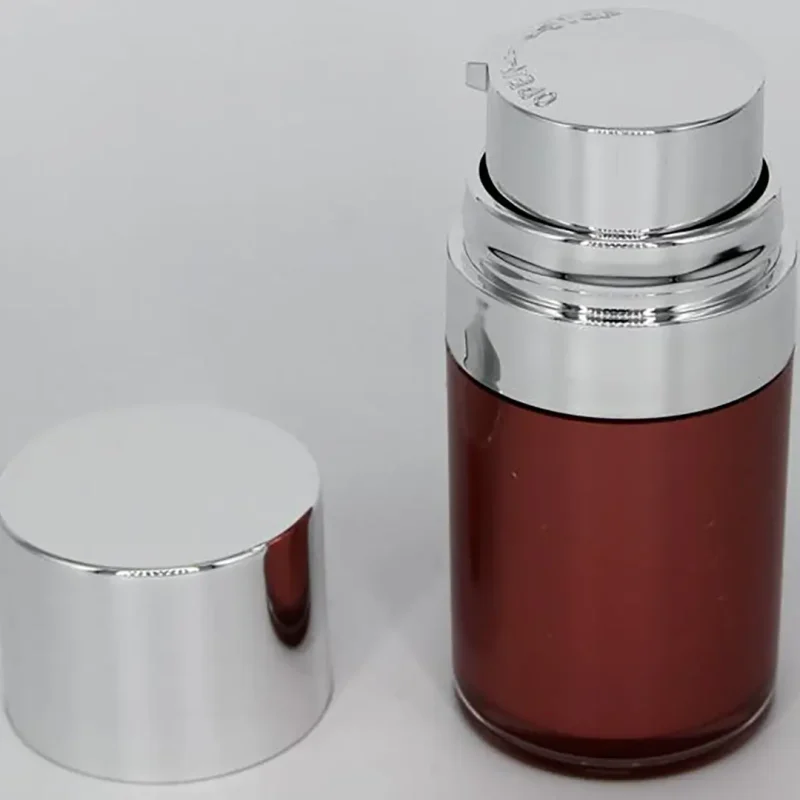A cylindrical cosmetic bottle with a metallic finish and a brown-tinted body. The bottle has a shiny silver cap that is removed and placed next to it on a white background. The top of the bottle is also silver and features a pump dispenser.