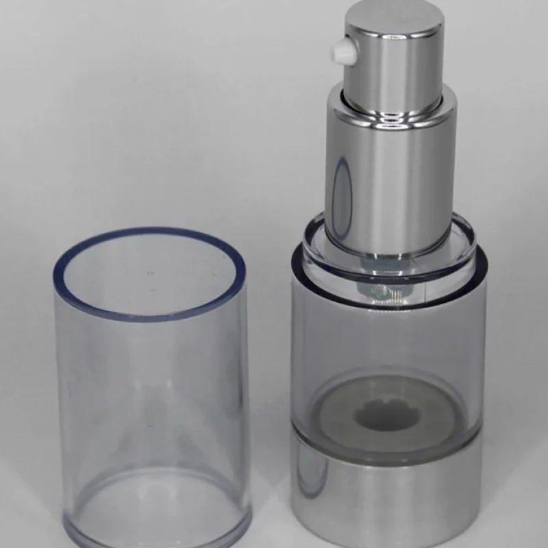 A silver and transparent airless pump bottle with its cap removed and placed beside it. The bottle is designed for dispensing liquid or cream products and is displayed against a plain white background.