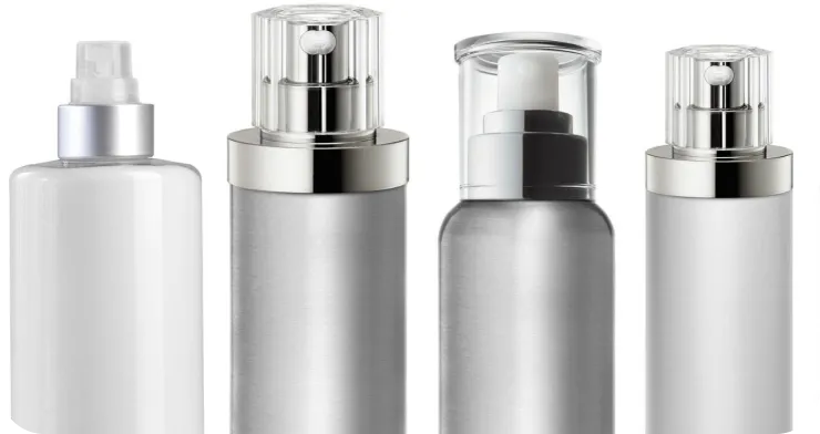 Four silver and white cosmetic bottles with pump and spray dispensers are lined up side by side. Each bottle features a sleek and minimalist design, with transparent and metallic caps.