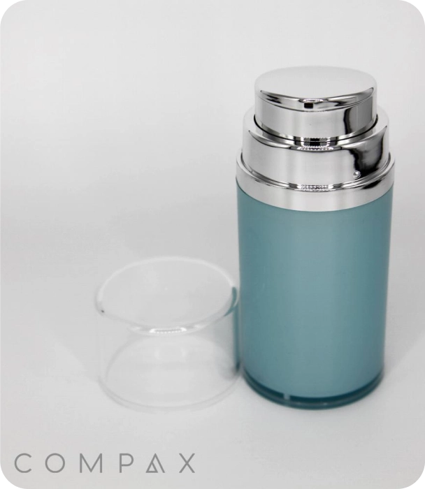 A sleek, blue cylindrical cosmetic container with a shiny silver pump top and a clear plastic cap placed beside it. The word COMPAX is displayed at the bottom left corner of the image.