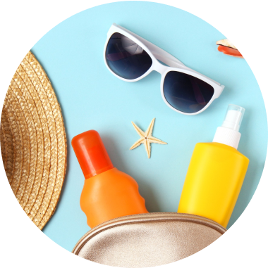 A beach-themed flat lay with a straw hat, white sunglasses, a starfish, sunscreen bottles in orange and yellow, and a golden cosmetic bag against a light blue background.