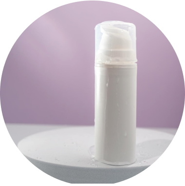 A white plastic pump bottle with a clear cap is placed on a round, white surface. The background features a soft purple gradient. Water droplets are visible on the bottle and surface, suggesting a fresh, clean look.