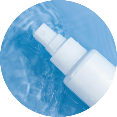 A close-up of a white spray bottle nozzle submerged partially in a pool of clear blue liquid. Water droplets are visible on the surface of the bottle and the surrounding liquid, giving a refreshing appearance.