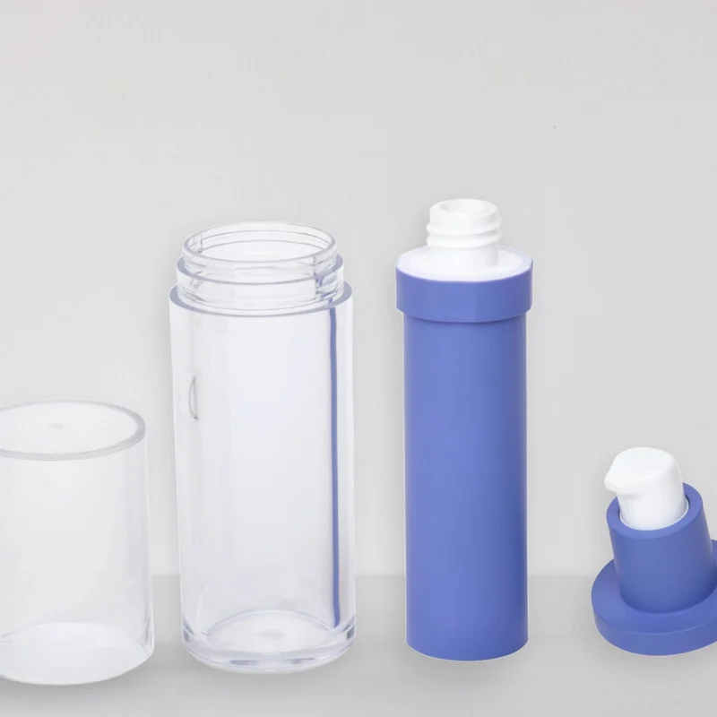 A clear cylindrical container with its transparent lid removed, revealing the open top. Beside it are a blue capsule-shaped container with its lid off and a blue pump dispenser head detached from a base, laid out on a light surface.
