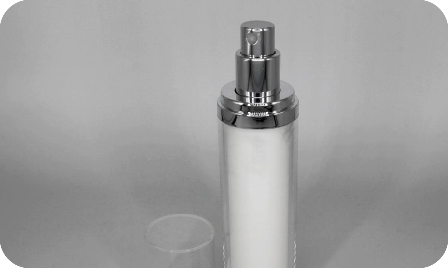 A silver and white cosmetic spray bottle with a shiny cap is centered against a plain gray background. The transparent lid is placed beside the bottle.